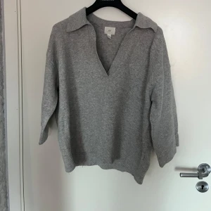 Grå stickad tröja med krage - Säljer en mysig grå stickad tröja med en snygg krage och v-ringning. Perfekt för kyliga dagar och passar både till vardags och lite finare tillfällen. Tröjan har långa ärmar och ribbade kanter för extra komfort.
