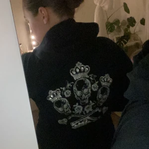 Svart zip upp Victoria's Secret🪽🖤 - Säljer en svart hoodie från Victoria's Secret i bra skick. Den har en cool design med dödskallar och kronor i silver på ryggen. Perfekt för höst och vinter med dragkedja framtill och långa ärmar. Superbekväm! ( det finns några diamanter som har försvunnit där bak )