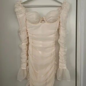 Champagnefärgad klänning från Oh Polly - Säljer en superfin champagnefärgad klänning från Oh Polly i storlek XS. Klänningen har en tight passform med volangdetaljer och långa ärmar. Perfekt för fest eller nyår! Den har en dragkedja i ryggen och är i ett syntetmaterial som ger en lyxig känsla. (Aldrig använd prislapp sitter kvar). pris går att diskuteras vid snabb affär