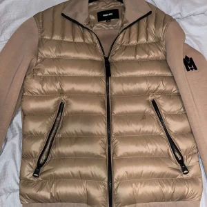 Beige pufferjacka från Mackage - Säljer en snygg beige pufferjacka från Mackage i storlek XS. Jackan har en dragkedja framtill och är quiltad för extra värme. Den har långa ärmar med ett coolt broderat märke på ena ärmen. Perfekt för höst och vår!