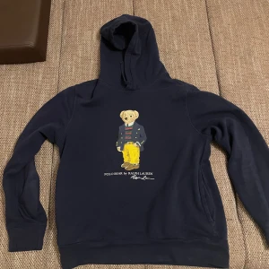 Ralph Lauren Bear  Hoodie - Säljer en snygg mörkblå hoodie från Ralph Lauren med en cool björn på framsidan. Perfekt för höst och vinter, den är både stilren och bekväm. Hoodien har långa ärmar och en klassisk passform. Perfekt för en avslappnad look! 🐻💙