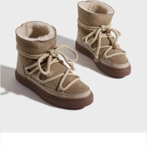 Beige vinterboots med snörning - Säljer ett par snygga beige vinterboots i mocka med fluffigt foder. De har en cool snörning som går runt hela skon och en stabil sula i brunt. Perfekta för kalla vinterdagar när du vill hålla stilen och värmen samtidigt. Passar både till vardags och lite mer uppklädda tillfällen. Knappt använda, nypris 2 999kr