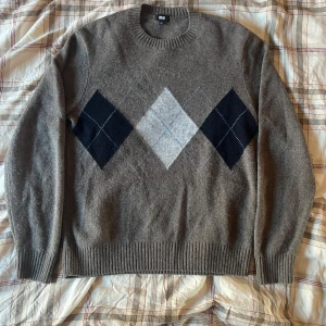 Kashmere tröja med argylemönster från Uniqlo - Säljer en snygg brun kashmere tröja från Uniqlo med klassiskt argylemönster i svart och grått på framsidan. Tröjan är i mycket bra skick och perfekt för höst och vinter. Den är stickad och har långa ärmar med ribbade muddar. Perfekt för en stilren och varm look!