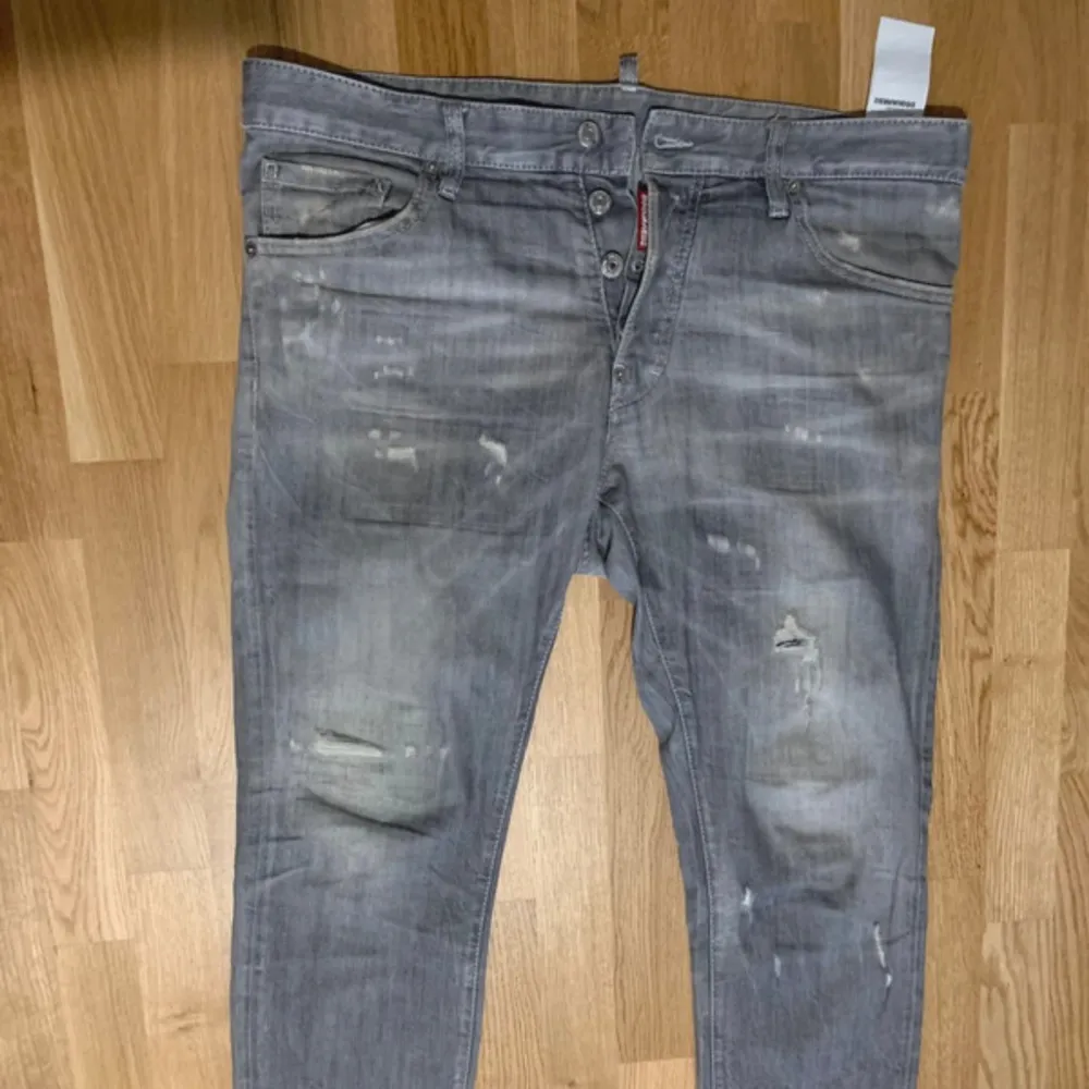 Säljer ett par grå jeans från DSQUARED2 i storlek 52. De har en sliten look med flera distinkta slitningar och en knappgylf. Perfekta för en avslappnad stil med en touch av edge. Tillverkade i Italien. Äkta!. Jeans & Byxor.