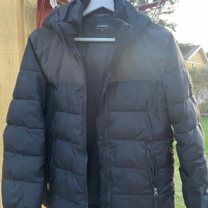 Svart pufferjacka från Everest  - Säljer en svart pufferjacka från Everest i bra skick. Jackan har en dragkedja framtill och två fickor med dragkedjor. Perfekt för kalla dagar med sin vadderade design och huva. Några små märken på baksidan, men inget som stör funktionen. Passar perfekt för höst och vinter! Storlek 152 men kan passa xs. 
