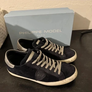 Philippe Model sneakers i svart mocka - Säljer ett par Philippe Model sneakers i svart mocka med grå snörning. Skorna har en klassisk design med en vit sula och är i bra skick. Perfekta för både vardag och festliga tillfällen.