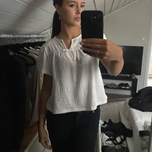 Vit blus med knytning - Säljer en söt vit blus i ett lätt och luftigt material. Den har korta ärmar och en fin knytning framtill som ger en romantisk touch. Perfekt för vår och sommar! Passar både till vardags och festliga tillfällen.