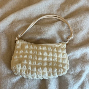 Beige/vit quiltad axelväska - Säljer en superfin beige/vit axelväska med quiltat mönster. Den har en praktisk dragkedja och en bekväm axelrem. Perfekt för att ge din outfit en mysig touch! 👜