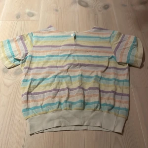 Randig tröja från Cristin Stevens - Säljer en färgglad randig tröja från Cristin Stevens. Den har korta ärmar och en bekväm passform. Perfekt för vår och sommar med sina pastellfärger i gult, lila, rosa och blått. Tröjan är i bra skick och redo för nya äventyr!