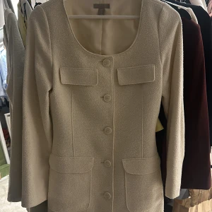 Offwit kavajklänning från H&M - Säljer en elegant beige kappa från H&M i storlek S.Den har en klassisk design med knappar framtill och två fickor. Perfekt för höst och vår, med en stilren look som passar både till vardags och fest. Kappan är i mycket bra skick och redo för en ny ägare!