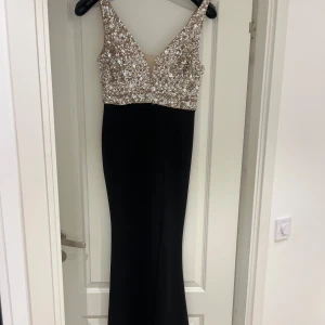 Svart långklänning med paljetter från Bubbleroom - Säljer en elegant svart långklänning från Bubbleroom. Den har en glittrig överdel med paljetter och en djup v-ringning. Perfekt för festliga tillfällen! Klänningen är i mycket bra skick och har en figurnära passform.
