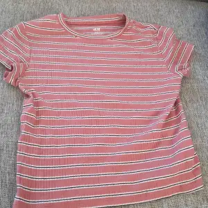 Säljer en söt rosa randig t-shirt från H&M Basic. Den har korta ärmar och är gjord i ett mjukt bomullsmaterial. Perfekt för vardagsbruk och passar bra till både jeans och shorts. T-shirten är i mycket bra skick och redo för en ny ägare!