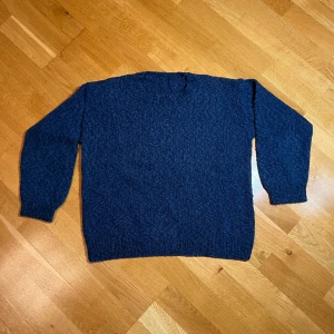 Mörkblå hemmastickad tröja - Säljer en mysig mörkblå hemmastickad tröja i bra skick. Perfekt för kalla höst- och vinterdagar. Tröjan har muddrade ärmar och en klassisk rund halsringning. Den är bekväm då den inte är stickig eftersom den är i bomull, idealisk för vardagsbruk eller en avslappnad dag hemma! 