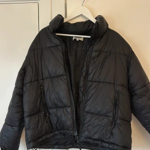 Svart pufferjacka från Weekday - Säljer en svart pufferjacka från Weekday i storlek S. Jackan har en cool oversized look med dragkedja framtill och två fickor med dragkedjor. Perfekt för kyliga höst- och vinterdagar. Den är i mycket bra skick och superbekväm att ha på sig. Passar både till vardags och lite mer uppklädda tillfällen.