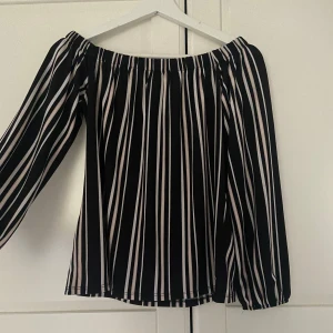 Randig offshoulder topp - Säljer en superfin randig offshoulder topp i svart och vit. Perfekt för sommardagar eller en kväll ute. Den har långa ärmar och en luftig passform som gör den bekväm att bära. Passar både till jeans och kjol för en stilren look.