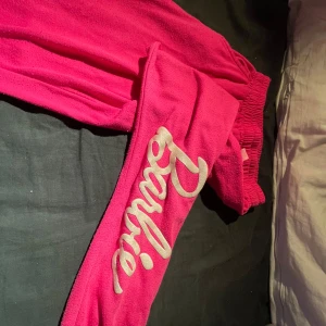 Rosa Barbie mjukisbyxor - Superfina rosa mjukisbyxor med Barbie-tryck längs benet. Perfekta för en mysig hemmakväll eller chill dag. Byxorna är i mjukt material och har en elastisk midja för extra komfort. De är i bra skick och redo för en ny ägare som älskar rosa och Barbie!🩷