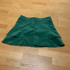 Grön lågmidjad manchesterkjol - Säljer en superfin lågmidjad grön manchesterkjol från att. i storlek 38. Kjolen har en cool volangdetalj och är perfekt för höst och vår. Den är i mycket bra skick!