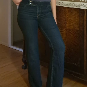 Mörkblå jeans från H&M - Säljer ett par mörkblå jeans från H&M Divided i storlek 42. De är low waist och har två knappar framtill samt att tyget är något stretchigt💓Jeansen har en klassisk bootcut fit och är perfekta för både vardag och fest. De är i bra skick och redo för en ny ägare!