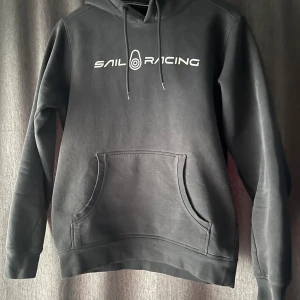 Svart hoodie från Sail Racing - Säljer en svart hoodie från Sail Racing i mycket bra skick. Den har en klassisk design med känguruficka och justerbar huva. Perfekt för både vardag och chill. Passar bra till jeans eller träningsbyxor. Hör av dig vid intresse!