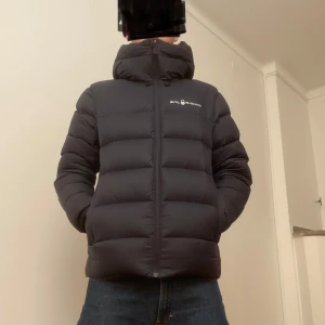 Mörkblå dunjacka från Sail Racing - Säljer en mörkblå dunjacka från Sail Racing i mycket bra skick. Jackan har en hög krage och dragkedja framtill. Perfekt för kalla vinterdagar med sin pufferdesign som håller värmen. Den har långa ärmar och en stilren look. Ny pris 7000kr