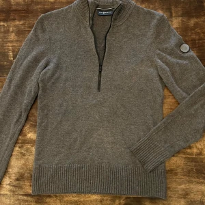 Stickad tröja från Sail Racing, stl S - Supersnygg grå stickad tröja i ullblanning med dragkedja i halsen från Sail Racing, rund logga på vänster arm. Storleken är vuxen S. Tröjan är mycket välbehållen och i gott skick.  Material: 50% ull 50% bomull 