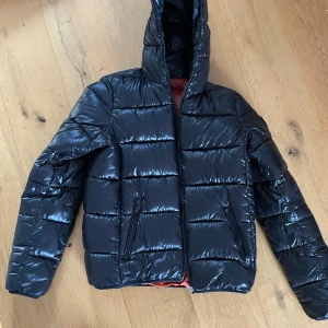 Svart pufferjacka från Save the Duck stl 16 år (XS/S) - Säljer en svart pufferjacka från Save the Duck i mycket bra skick. Inga tecken på användning. Jackan är ultralätt och har en snygg orange insida. Perfekt för höst och vinter med huva för extra värme. Passar både till vardags och lite finare tillfällen. 🖤🧡