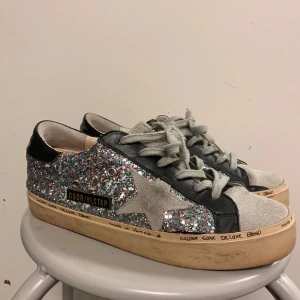 Glittriga sneakers från Golden Goose - Säljer ett par unika Golden Goose sneakers i glittrigt material. Skorna har en cool stjärndetalj på sidan och är i en mix av silver och rosa glitter. De har en vintage-look och grå snörning. Perfekta för att sticka ut i mängden! Har två defekter på sulan, se de två sista bilderna. Utöver i gott skick och defekterna är inget man stör sig på. Kontakta gärna men kö nu går också bra💗