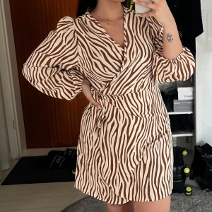 Zebramönstrad omlottklänning - Säljer en superfin zebramönstrad omlottklänning i beige och brun. Klänningen har långa puffärmar och en smickrande omlott-design som knyts i midjan. Perfekt för både vardag och fest! 🦓✨