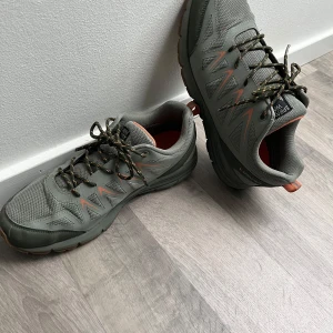 Gröna sneakers från Sprayway - Säljer ett par gröna Sprayway sneakers i mycket bra skick. De har en robust sula och snörning i matchande färger. Perfekta för utomhusaktiviteter med bra grepp och komfort. De har orange detaljer som ger en snygg kontrast.