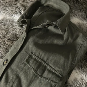Grön overshirt - Säljer en snygg grön overshirt i bra skick. Den har en klassisk krage och knappar framtill. Perfekt för lager-på-lager-stilen under hösten eller våren. Passar både till vardags och lite mer uppklädda tillfällen. Skön och stilren! Märket har jag ingen aning om då lappen tyvärr är borta! Därför säljs den också till bra pris. Str S i bra skick!