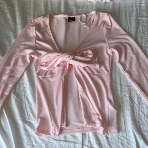 Rosa långärmad topp från Gina Tricot - Säljer en söt rosa långärmad topp från Gina Tricot i storlek XS. Toppen har en v-ringad design med en knytning framtill som ger en fin detalj. Perfekt för vår och sommar! 🌸 tröjan är helt ny endast testad.