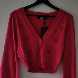 Rosa kofta med hjärtmönster från Heartbreak - Rosa kofta från Heartbreak med söta hjärtan som mönster. Den är croppad och har en v-ringad design med knappar framtill. Aldrig använd. Storlek: S  Skickas inslagen i silkespapper i vattentätt paket.   Skicka pm för fler bilder. 