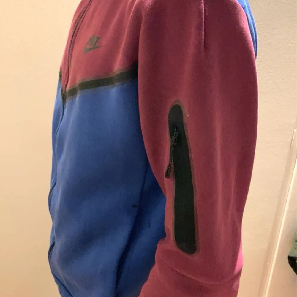 Säljer en snygg blå och vinröd Nike tech  hoodie i storlek S. Hoodien har en dragkedja framtill och en praktisk ficka med dragkedja på ärmen. Perfekt för höst och vår med sin sportiga stil och bekväma passform.. Tröjor & Koftor.