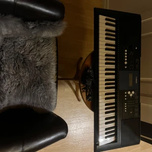 Yamaha keyboard med tillbehör - Säljer ett Yamaha keyboard i svart med vita tangenter. Det har en digital display och flera kontrollknappar för olika funktioner. Perfekt för både nybörjare och erfarna musiker. Strömkabel ingår. Passar bra för hemmabruk eller mindre spelningar.