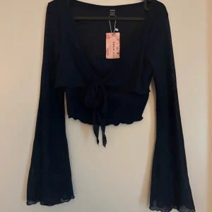 Svart långärmad topp med knyt - Säljer en snygg  långärmad topp med knyt framtill. Den är croppad och har en v-ringad design som ger en stilren look. Perfekt för fest eller en utekväll!