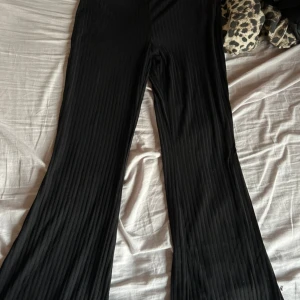 Svarta ribbade byxor från H&M - Säljer ett par svarta ribbade byxor från H&M i storlek M. Byxorna har en hög midja och en loose passform med en snygg bootcut-stil. Perfekta för både vardag och fest! 🖤