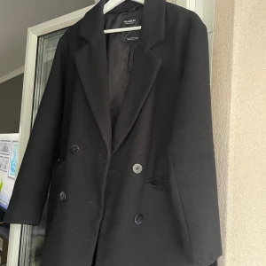 Svart kappa från Pull&Bear - Säljer en stilren svart kappa från Pull&Bear i storlek XS. Den har en klassisk design med knappar framtill och ett bälte i midjan för en snygg passform. Perfekt för höst och vår! 🖤