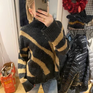 Svart och beige stickad tröja - Säljer en supermysig svart och beige stickad tröja med ett coolt mönster. Den har en hög krage och långa ärmar, perfekt för kyliga dagar. Tröjan är i bra skick och passar perfekt till jeans för en avslappnad look. Perfekt för höst och vinter! Som sagt bra skick förutom lite sliten och lite slitage vid halsen där kragen blivit lite lös ❤️