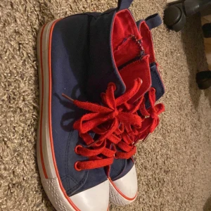 Blå och röda sneakers med snörning - Säljer ett par coola sneakers i blått och rött med vita detaljer. Skorna har en klassisk design med snörning och en vit tåhätta. Perfekta för vardagsbruk och ger en färgklick till din outfit. De är i bra skick och redo för nya äventyr!