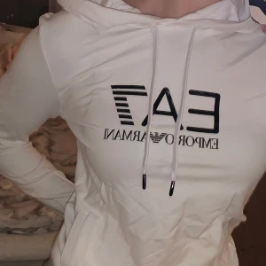 Vit hoodie från Emporio Armani - Säljer en vit hoodie från Emporio Armani med deras ikoniska logga tryckt på framsidan. Huvan har dragsko och materialet är mjukt.