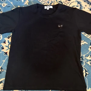 Svart t-shirt från Comme des Garçons - Säljer en svart t-shirt från Comme des Garçons med det ikoniska hjärta med ögon broderat på bröstet. T-shirten är i bomull och har en normal passform med korta ärmar. Perfekt för en stilren och enkel look. 🖤Pris 300kr. Möts upp i Stockholm eller fraktas