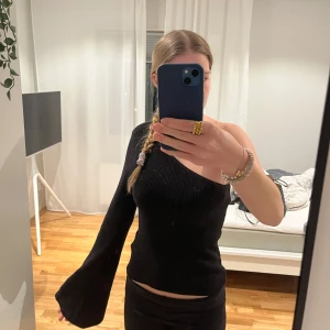 Svart oneshoulder topp - Säljer en snygg svart oneshoulder topp med lång ärm. Den är ribbad och har en tight passform som sitter perfekt för festliga tillfällen. Materialet är mjukt och stretchigt, vilket gör den bekväm att bära hela kvällen. Perfekt för att styla med ett par jeans eller en kjol! Den är glittrig och passar perfekt till fest eller nyår, men även vardag!