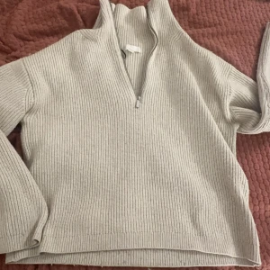 Beige ribbad tröja med dragkedja - Säljer en stilren beige ribbad tröja med dragkedja och hög krage. Perfekt för kyligare dagar och enkel att matcha med olika outfits. Tröjan har långa ärmar och en bekväm passform.