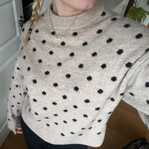 Beige prickig stickad tröja - Säljer en mysig beige stickad tröja med svarta prickar, från H&M i storlek XS. Tröjan har långa ärmar och en ribbad kant vid ärmslut och nederkant. 
