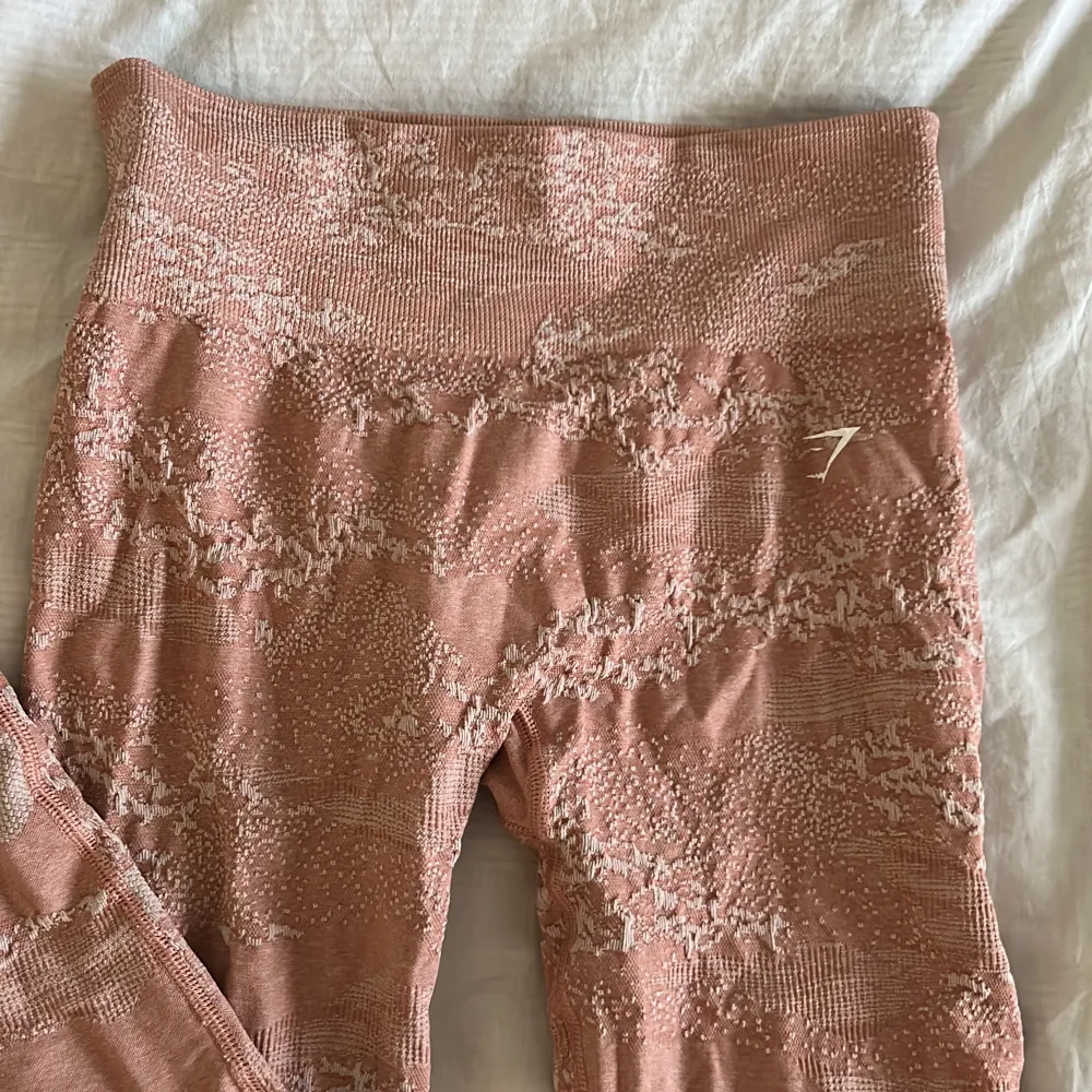 Snygga rosa leggings från Gymshark med ett unikt mönster. De är högmidjade och har en tight passform, perfekta för träning eller en aktiv vardag. Materialet är stretchigt och bekvämt. Storlek M. Farkut & Housut.
