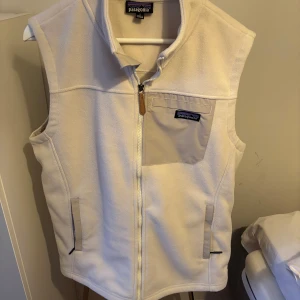 Vit fleeceväst från Patagonia - Säljer en stilren vit fleeceväst från Patagonia med dragkedja och bröstficka. Perfekt för lager-på-lager under kyliga dagar. Västen är aldrig använd, skick - 10/10. Storleken är S men skulle nog passa något större personer!