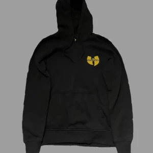 Svart hoodie från Wu-Wear - ✅Säljer en svart hoodie från Wu-Wear med det ikoniska Wu-Tang Clan-logotypen i gult på bröstet.✅Hoodien har en klassisk passform med känguruficka och justerbar huva. Perfekt för fans av Wu-Tang!💸 Priset är diskuterbart!💸