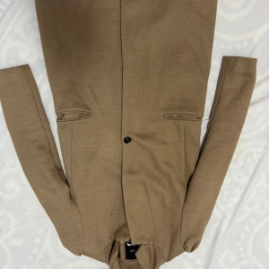 Beige kappa från Mango - Säljer en stilren beige kappa från Mango i mycket bra skick. Den har en klassisk design med knappar framtill och långa ärmar. Perfekt för höst och vår, och ger en elegant touch till vilken outfit som helst. Passar både till vardags och festliga tillfällen.