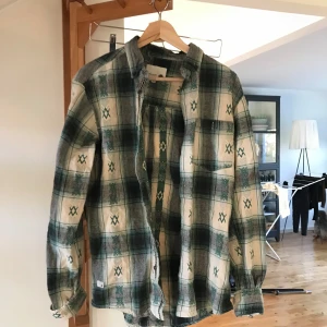 Rutig skjorta från Humör - Säljer en snygg rutig skjorta från humör i grönt och vitt. Skjortan har långa ärmar och ett klassiskt rutmönster med unika detaljer. Perfekt för höst och vår, och funkar både till vardags och fest. Den är i bra skick och redo för nya äventyr!