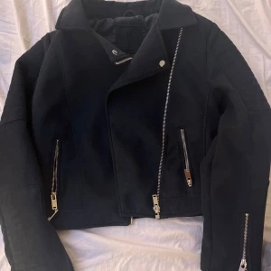 Svart jacka  med dragkedjor - Snygg svart jacka med asymmetrisk dragkedja och flera dragkedjedetaljer. Jackan har en klassisk krage och är perfekt för en edgy look. Passar bra till både jeans och klänning.